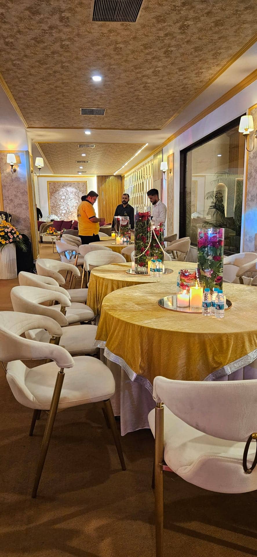 Round private dining tables with gold cloths and cream chairs beside a window wall