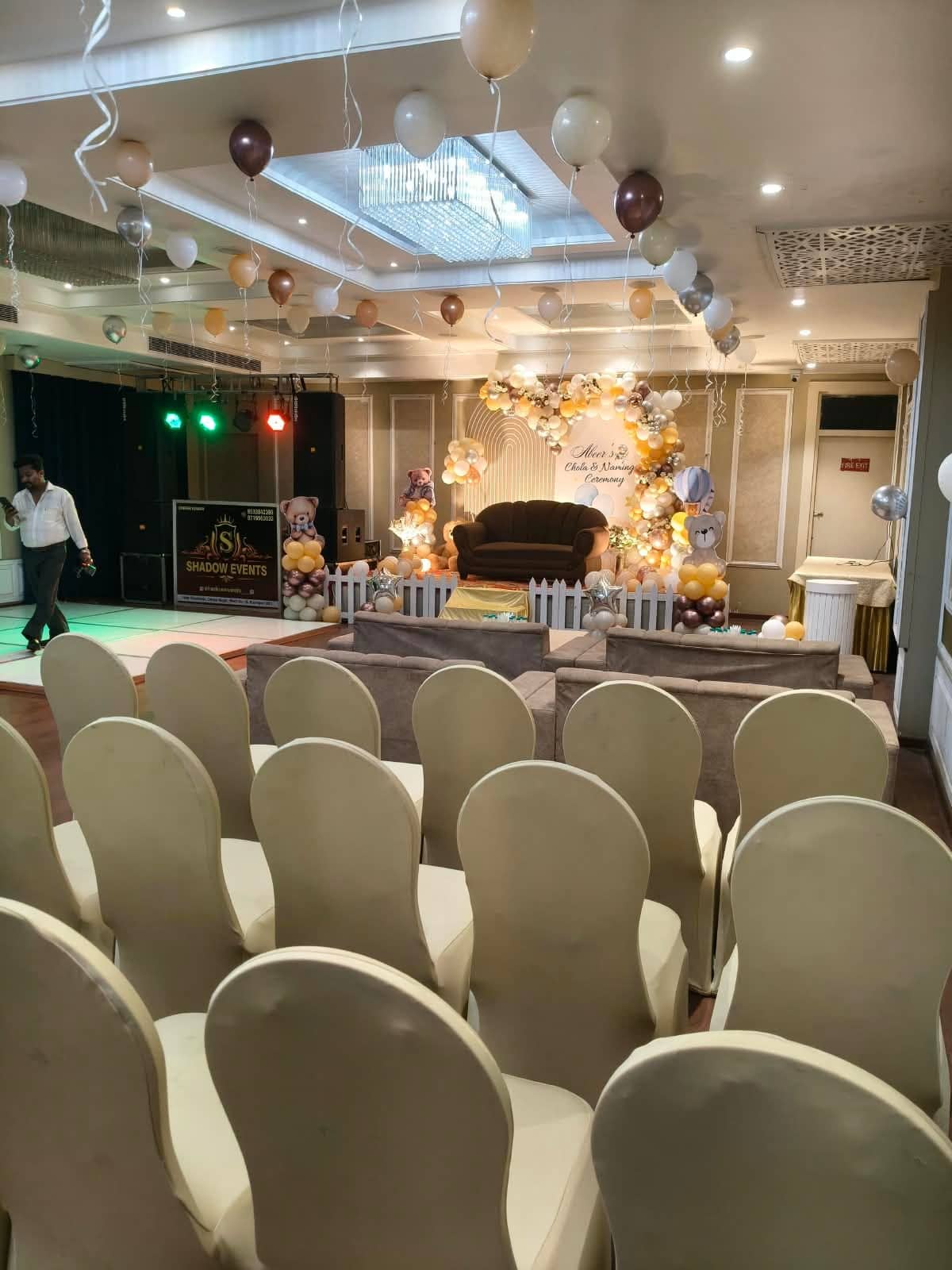 Banquet rounds with covered chairs laid out facing a decorated stage in a large carpeted hall