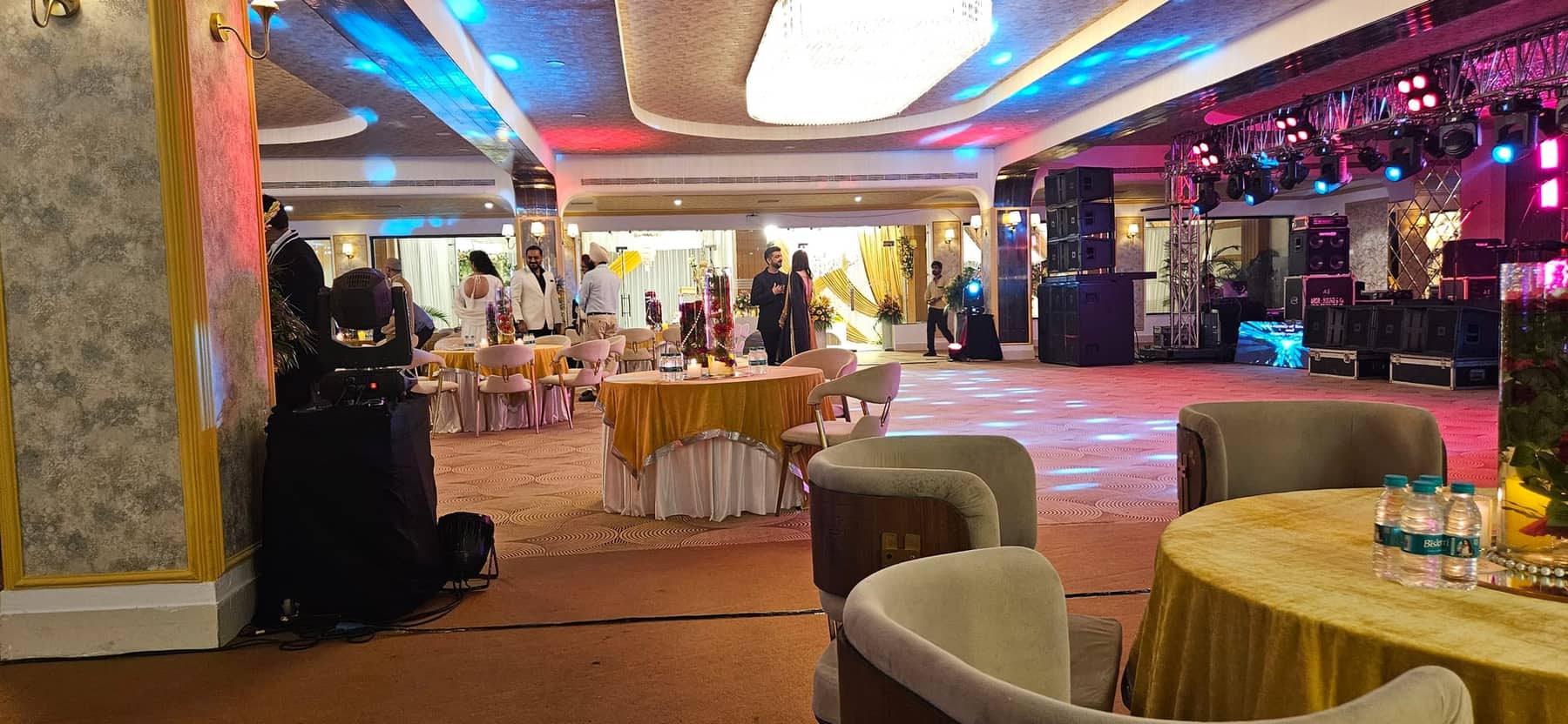 Guests seated at round tables in the banquet hall during an evening function, with the stage lit behind them