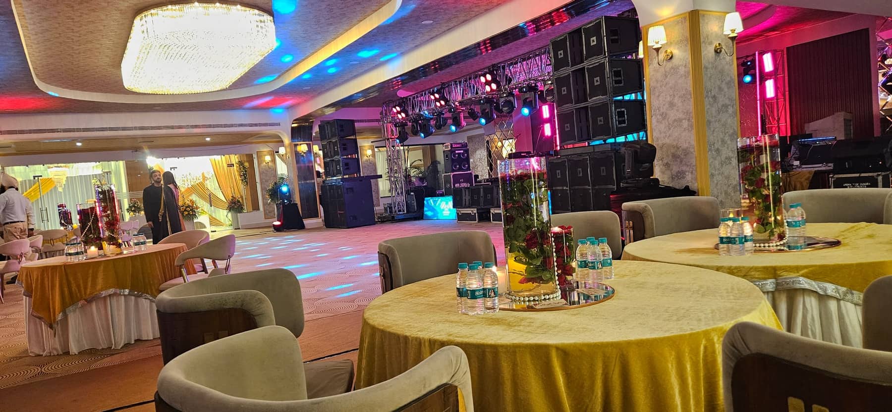 A banquet hall with round tables under a large crystal chandelier, with a buffet counter along one side