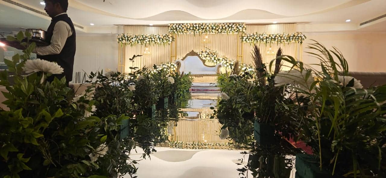 A ceremony aisle lined with potted palms leading to a flower-dressed stage