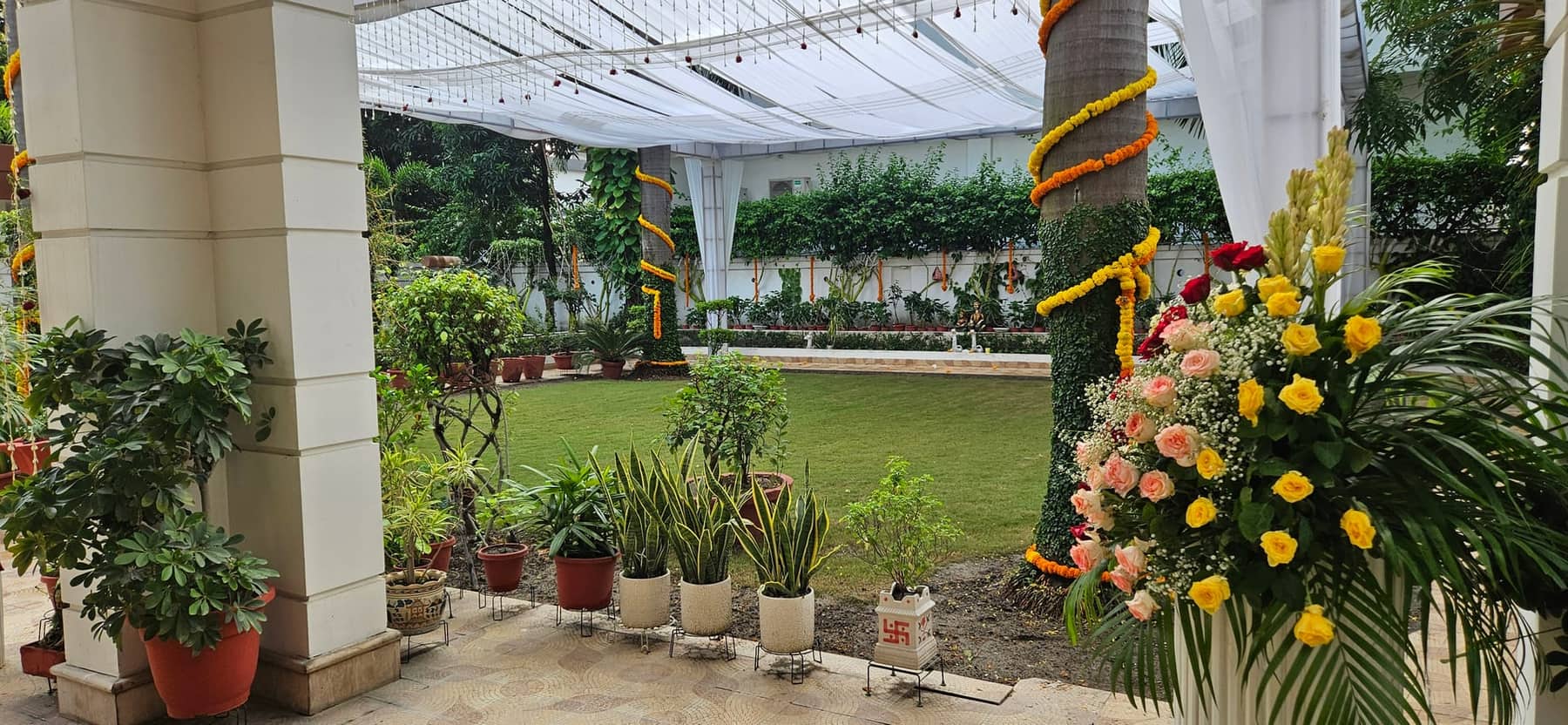 A garden lawn beside the hotel's colonnade, with potted palms and a marigold arrangement on a plinth
