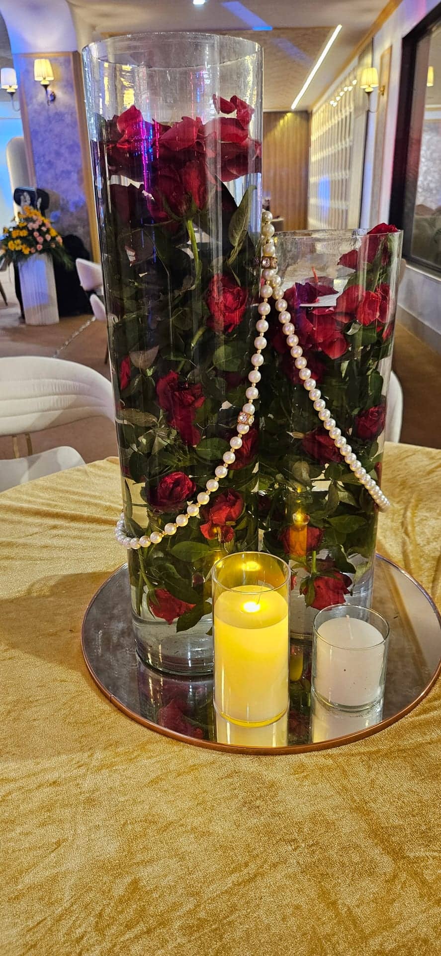 A private dining table with a gold cloth, a mirrored centrepiece of orchids and roses, and a lit candle
