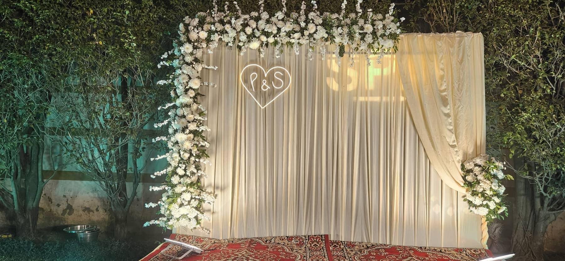 A reception stage with a floral backdrop carrying a couple's monogram above a soft seating arrangement
