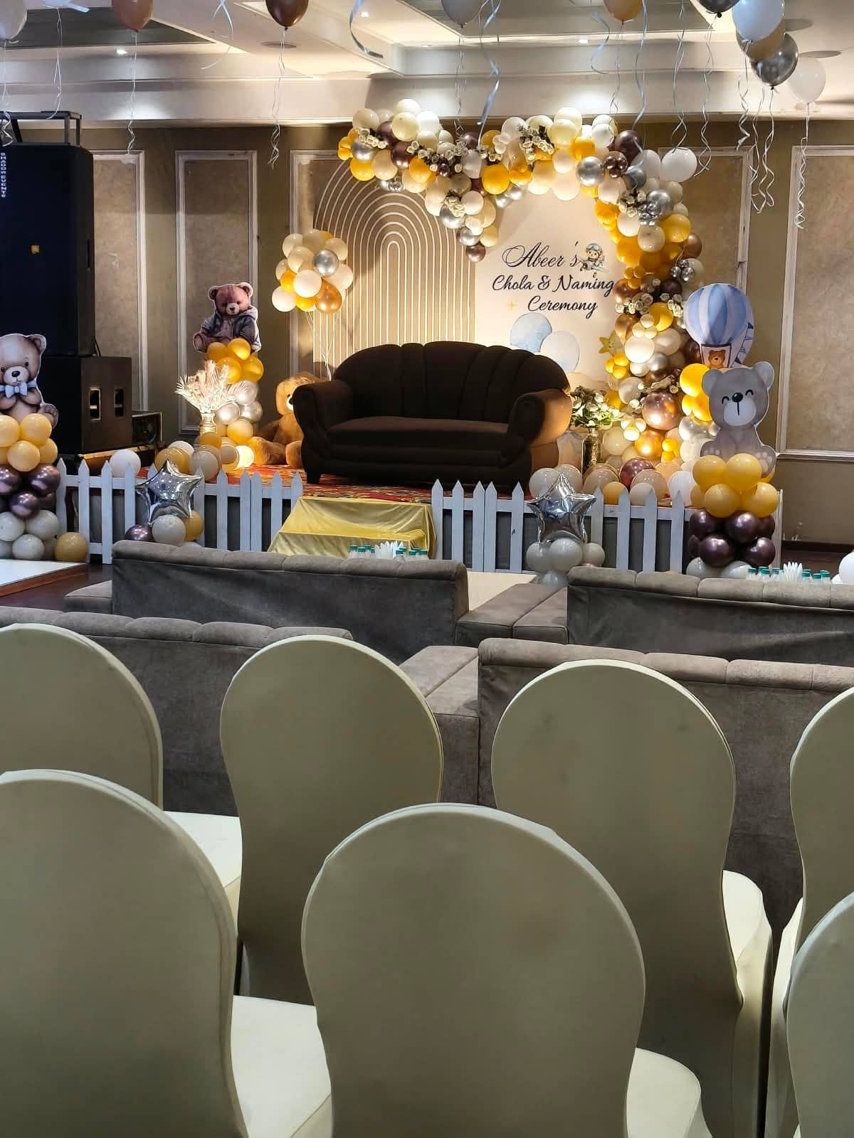 A reception stage framed by a gold and floral arch with covered chairs arranged in rows in front