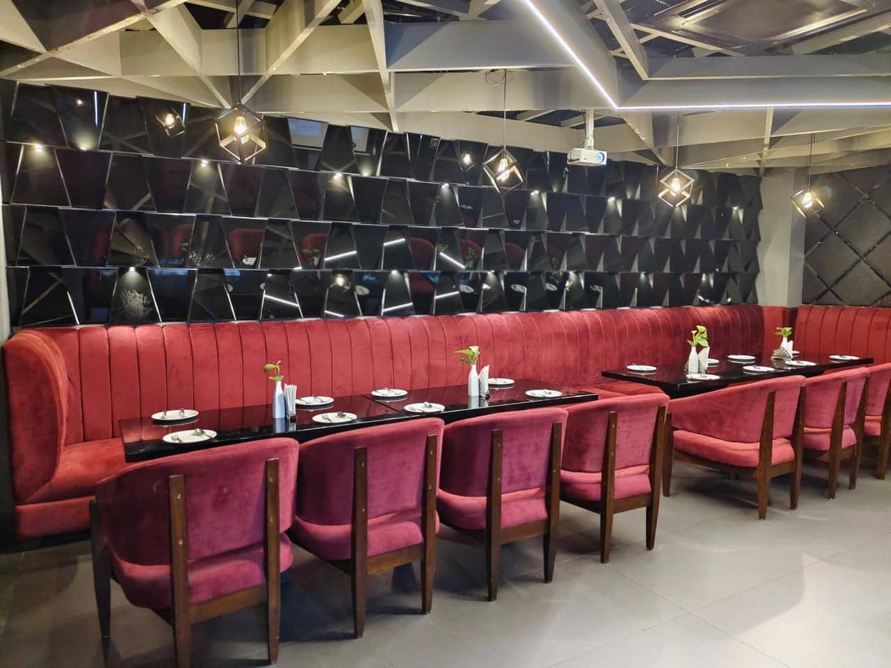 A dining area with banquette and booth seating in red velvet below a panelled, mirrored wall